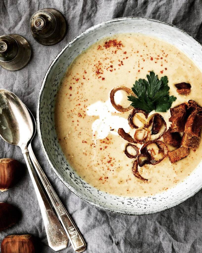 Creamy chestnut soup garnished with crispy onions, fresh parsley, and a sprinkle of spices.