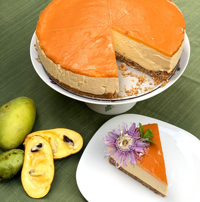 Pawpaw cheesecake with orange glaze, served with fresh pawpaw fruit and edible flower garnish.
