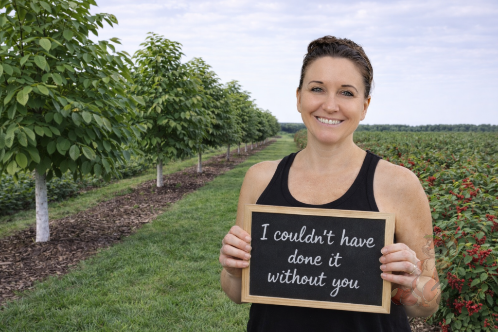 Heather standing between American Pawpaw trees and red currants holding a sign thanking the Nuts About Dee’s Berries Supporters