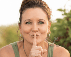 Heather Brown holding a finger to her lips in a "shh" gesture, teasing a major upcoming announcement from Nuts About Dee's Berries.