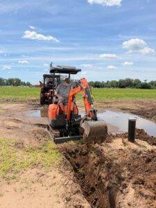 Mini excavator digging near the well during installation of the orchard irrigation system at Nuts About Dee's Berries.
