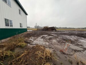 Completed farm septic installation with backfilled and graded soil beside the Nuts About Dee's Berries farm building in Brodhead, Wisconsin.